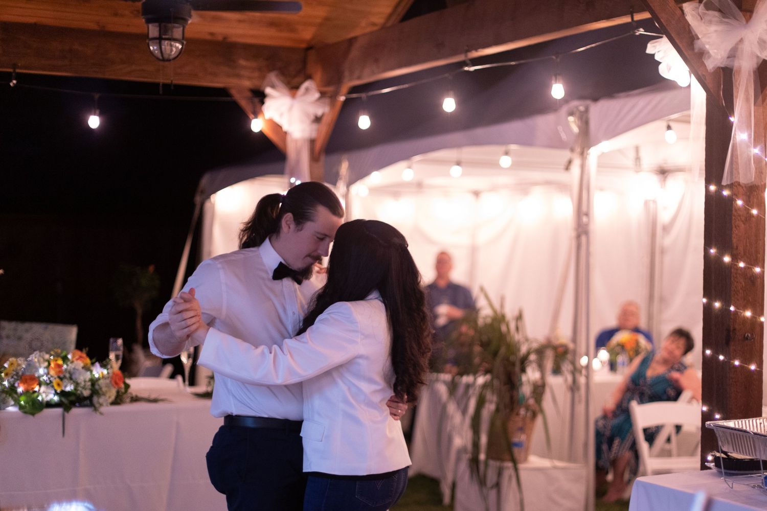 Couples dancing at a wedding reception under string lights and white tent coverings.