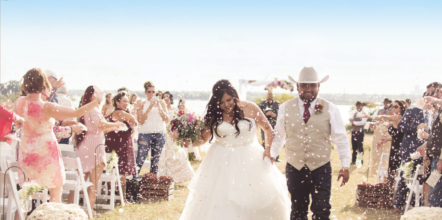 Bride and groom walk joyfully through cheering guests throwing confetti at outdoor western wedding.