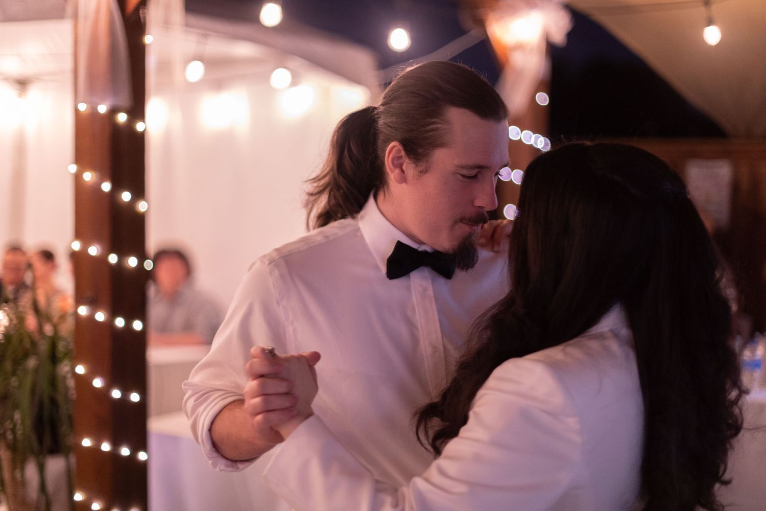 A romantic dance moment captured at a reception with string lights and floral decorations.