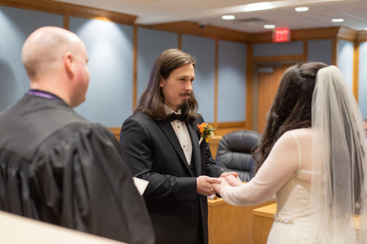 A couple exchanges rings during their courthouse wedding ceremony with a judge present.