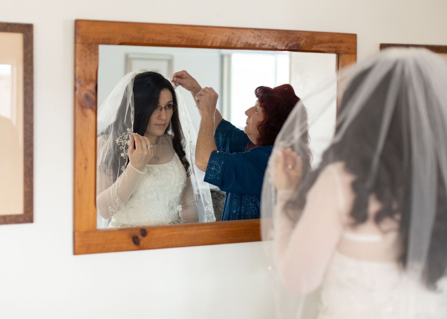 A bride getting her veil and hair styled in front of a wooden framed mirror.