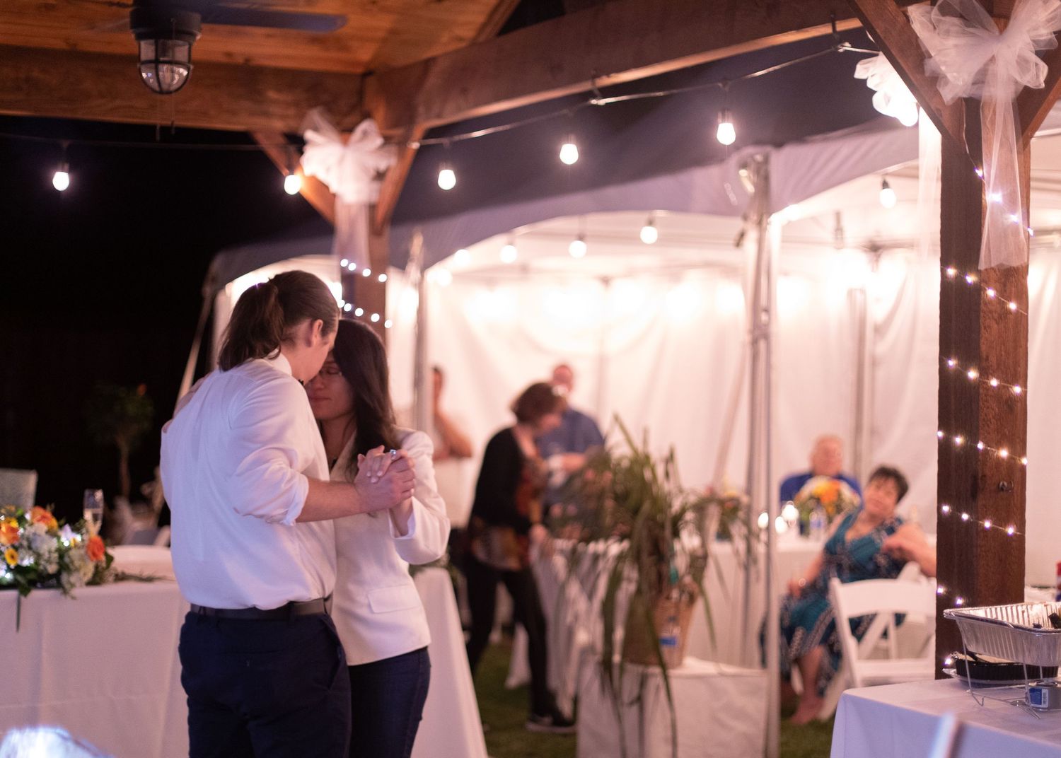 A couple dancing under string lights at an outdoor wedding reception venue.