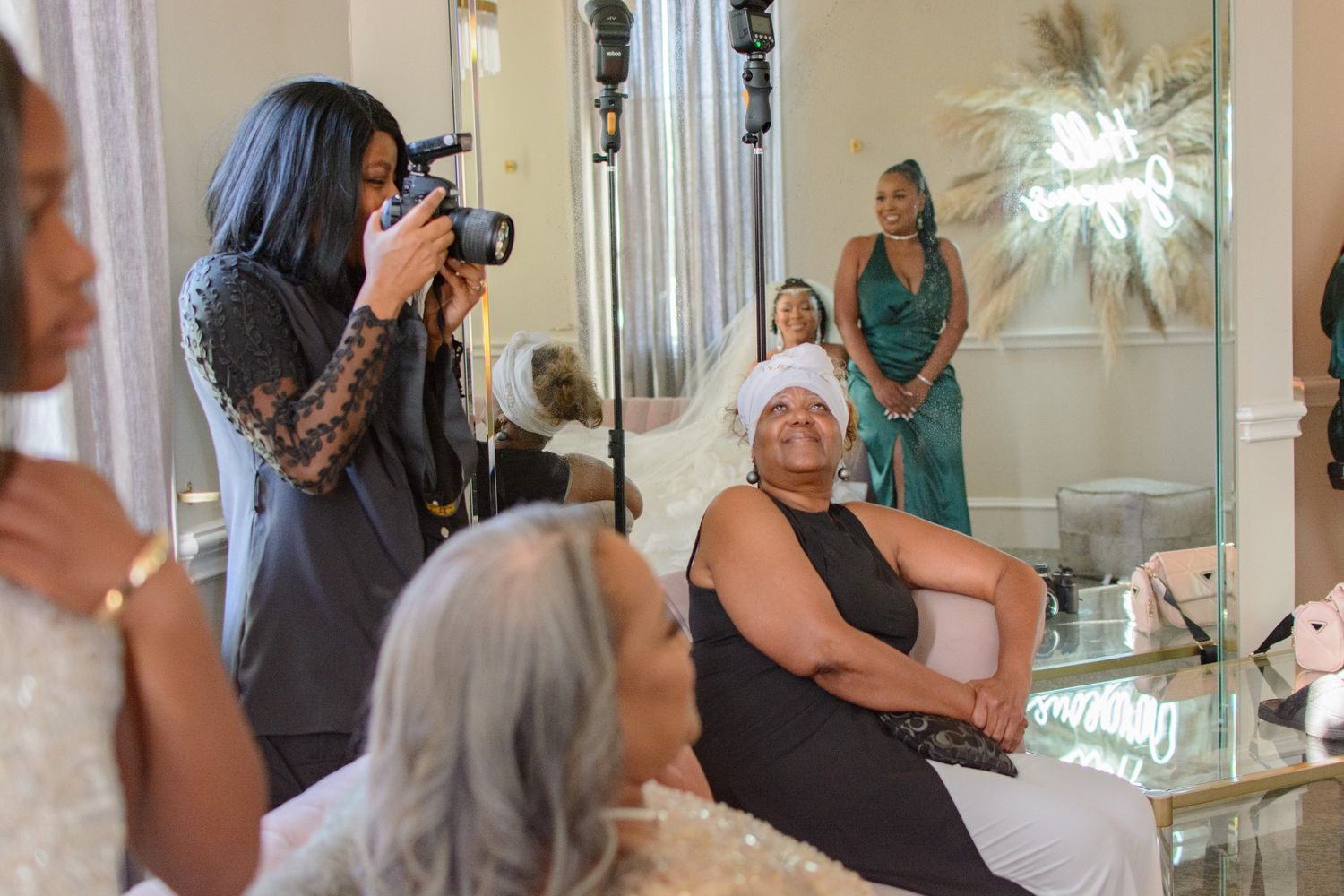 Photographer capturing bride getting ready in a mirror-lined dressing room with guests watching.