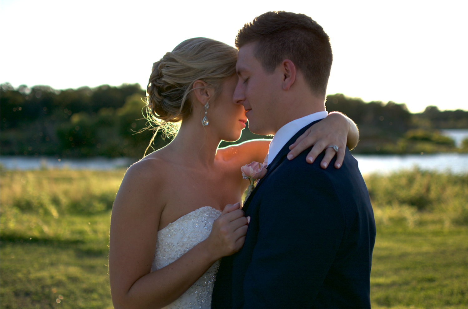 Bride and groom share an intimate golden hour moment near a scenic lakeside at sunset.