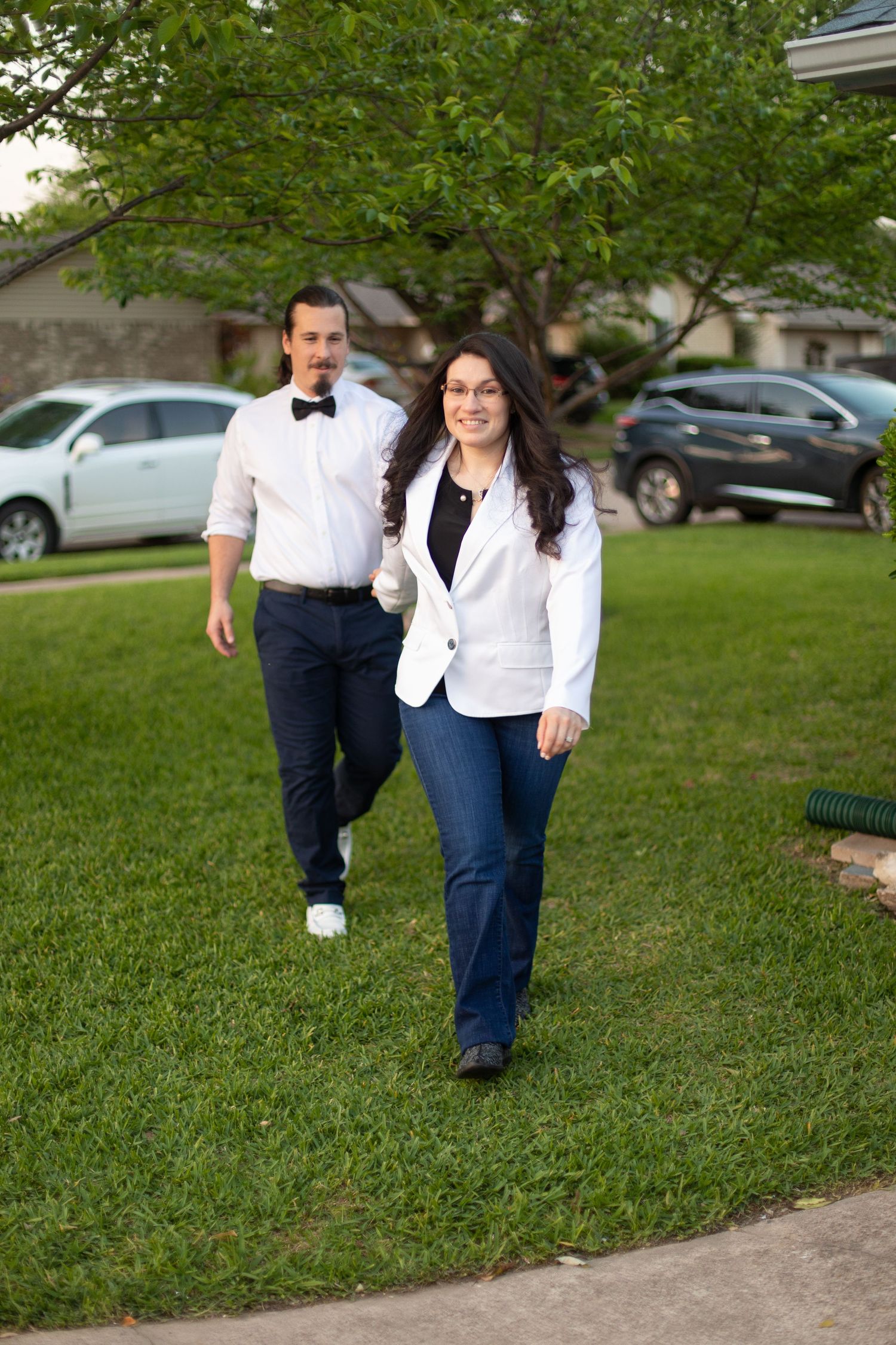 A couple in coordinated white and navy outfits walking on a grassy lawn.
