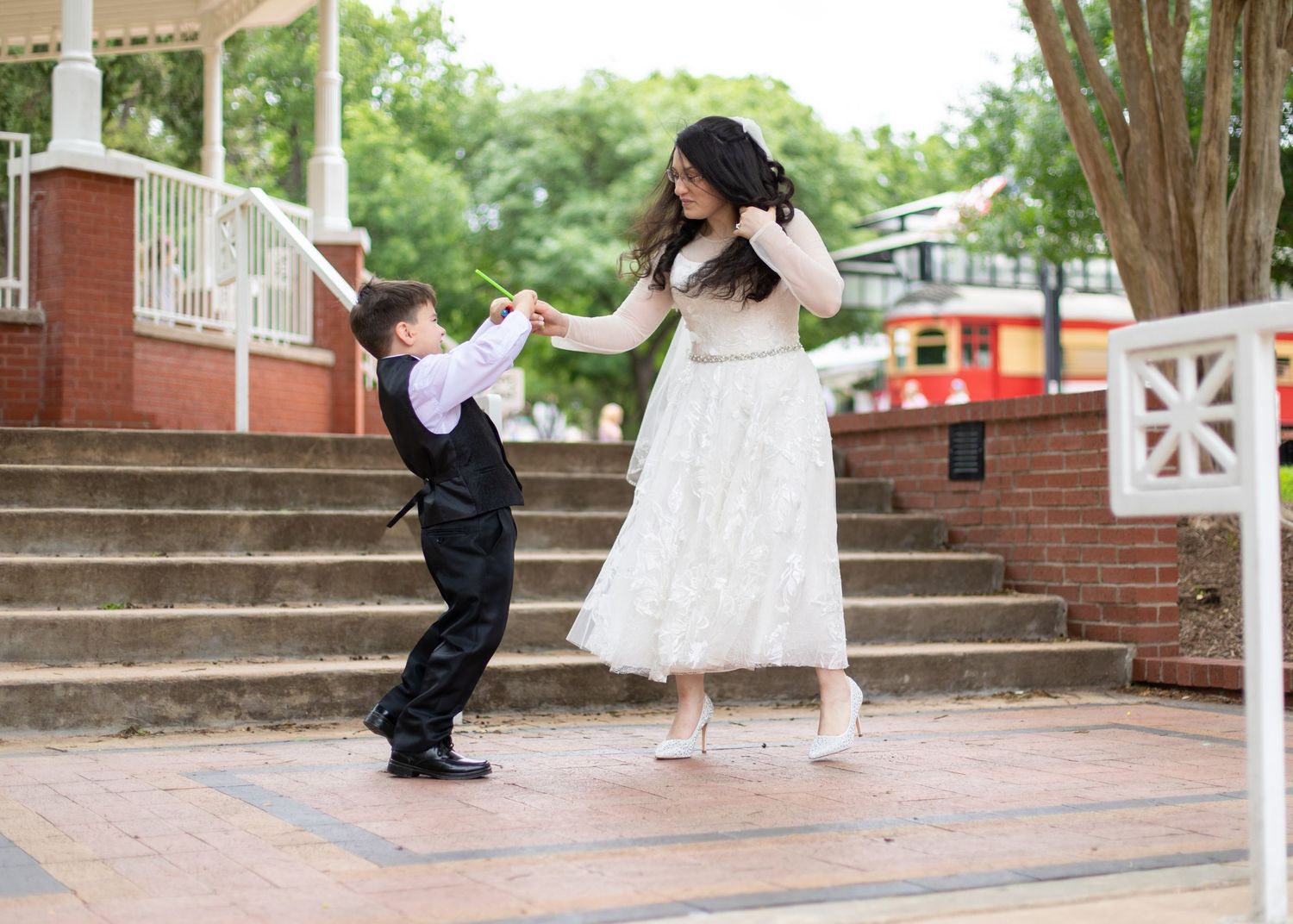 Bride and ring bearer share playful dancing moment on brick steps during wedding celebration.