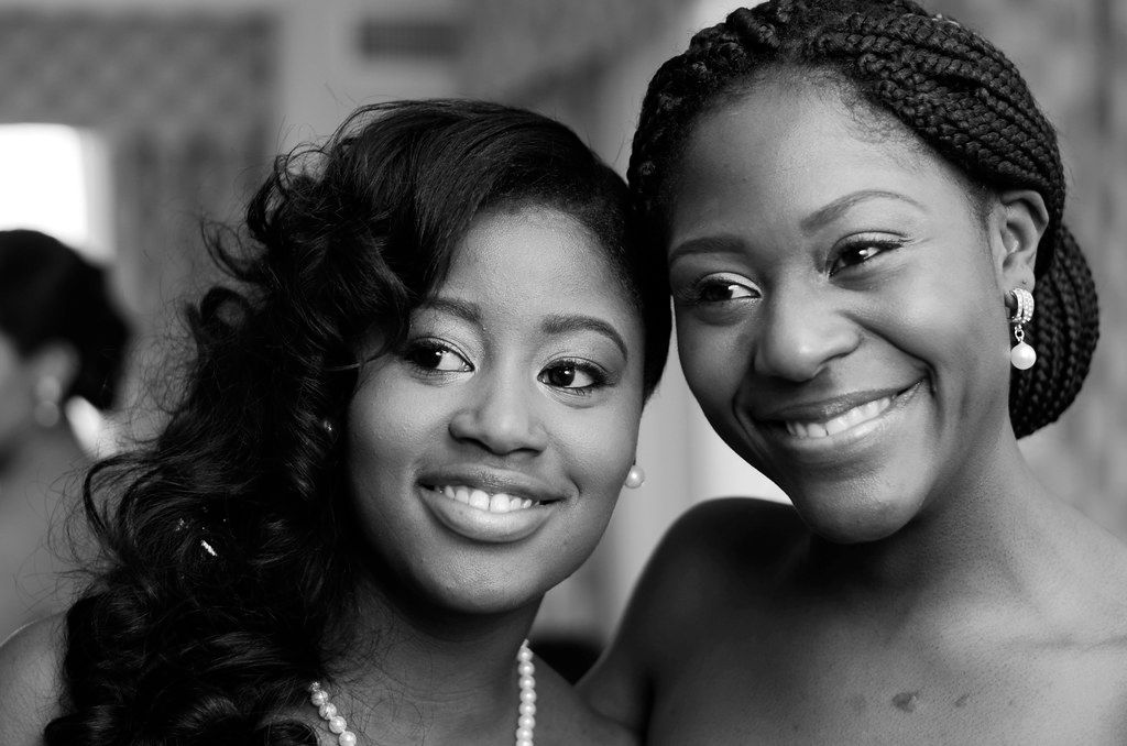 Two smiling women pose together in a black and white close-up portrait at a wedding celebration.