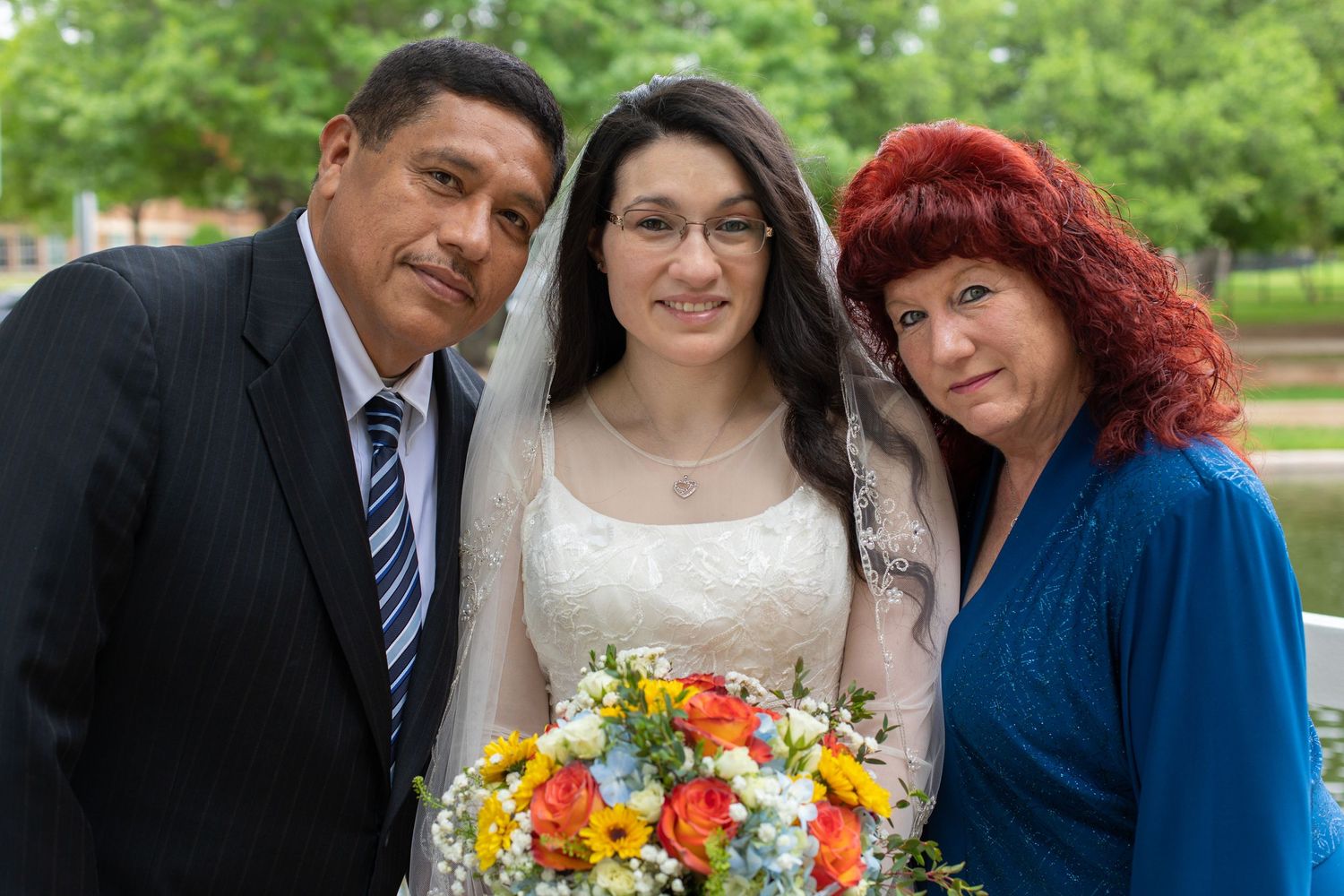 A wedding portrait with bright floral bouquet against lush green outdoor backdrop.