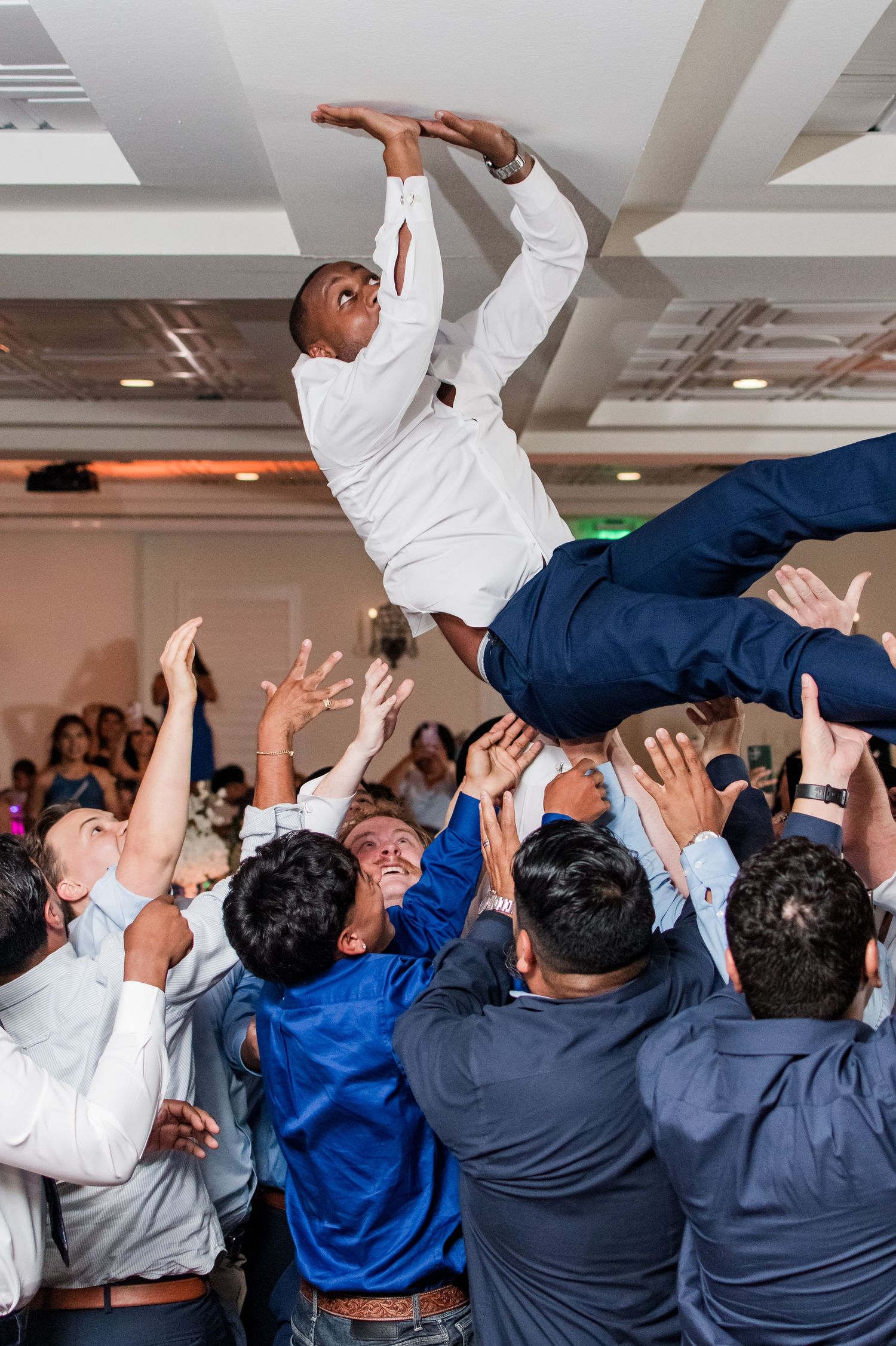 Groomsmen tossing groom into the air during a lively wedding reception celebration.