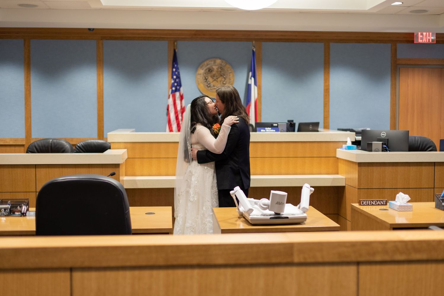 A couple embraces after their courthouse wedding ceremony in front of the judge's bench.