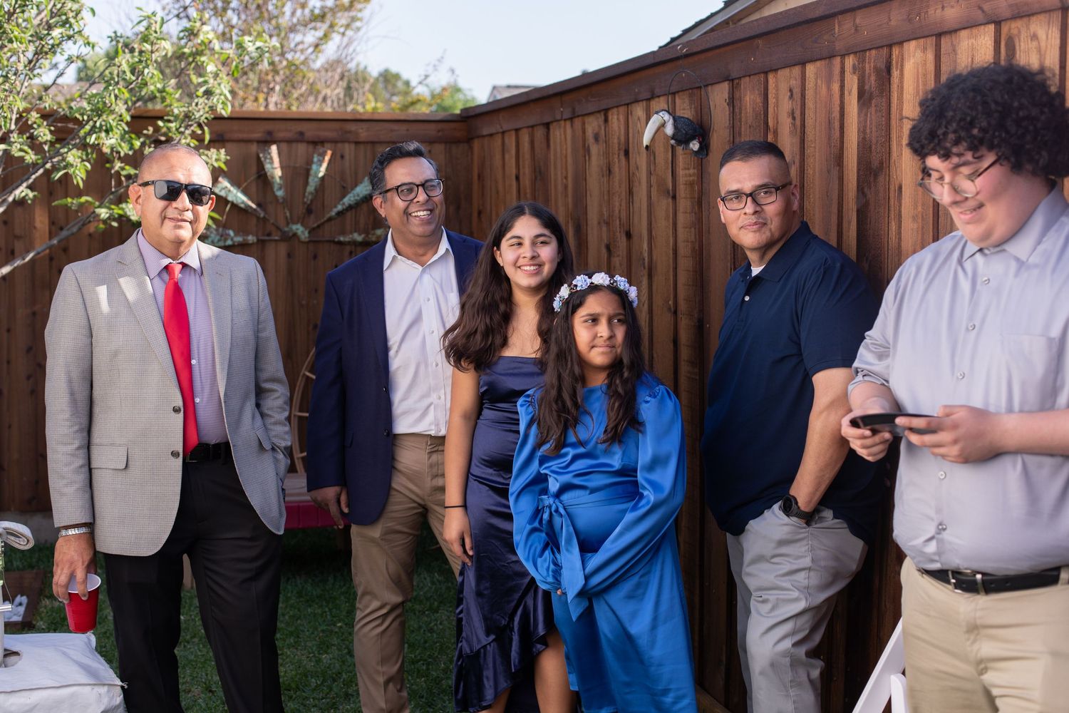 Group photo of wedding guests standing against wooden fence in outdoor setting.