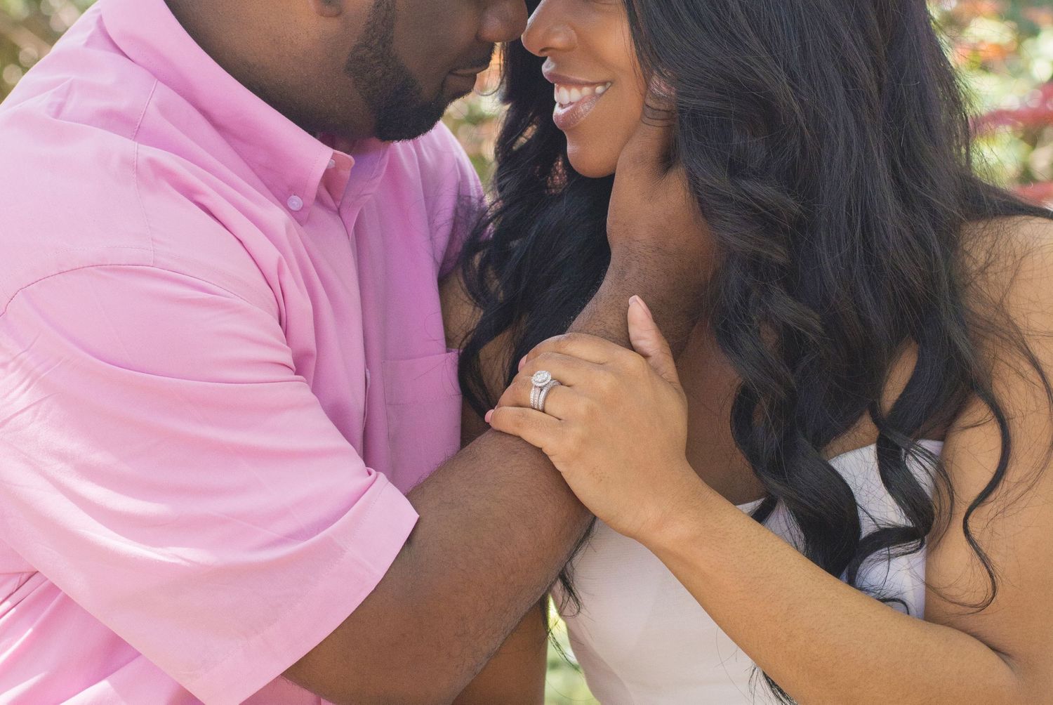 Close-up shot of a couple's hands showing off an engagement ring in an outdoor setting.
