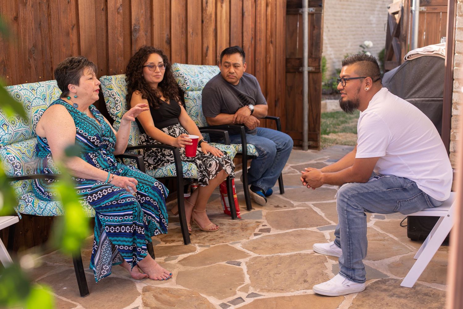 People sitting and conversing on a stone patio with decorative furniture.