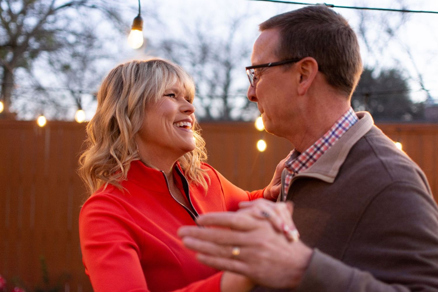 Couple dancing together outdoors at dusk with string lights in background.