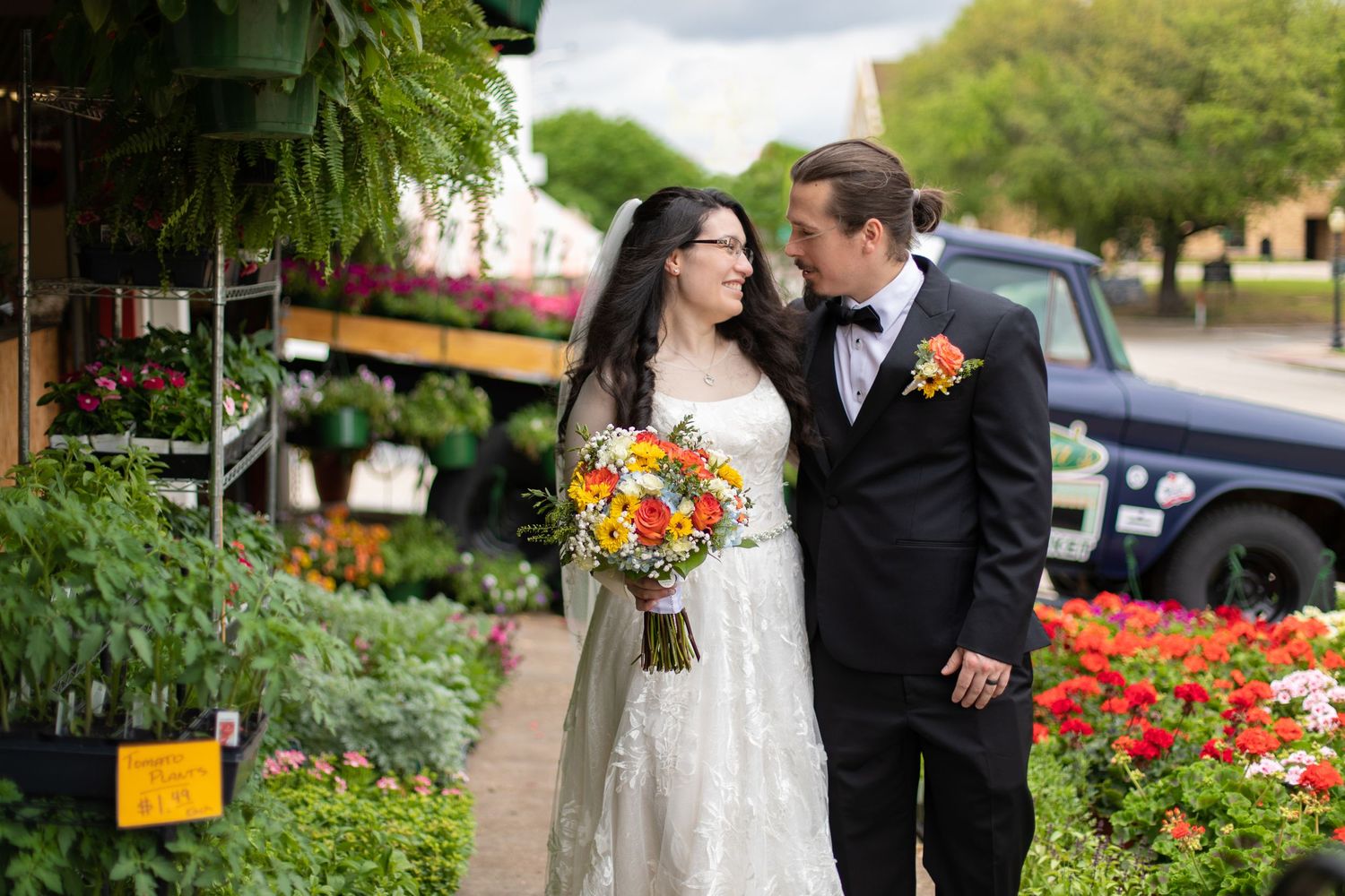 A couple poses for a portrait in front of colorful flower displays at a garden center.