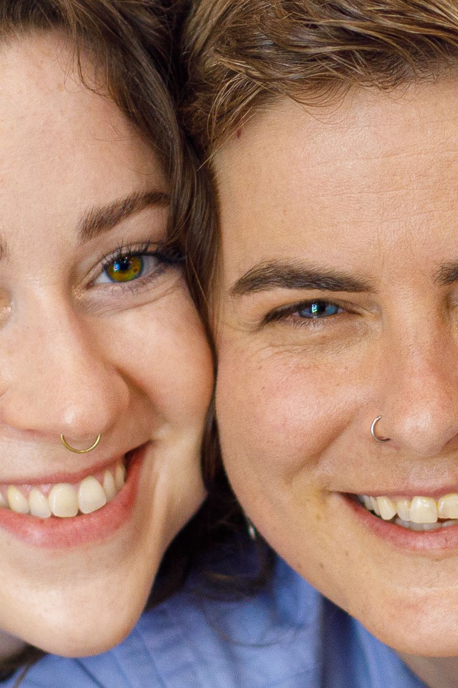Close-up portrait of two smiling women with nose rings cheek to cheek outdoors.