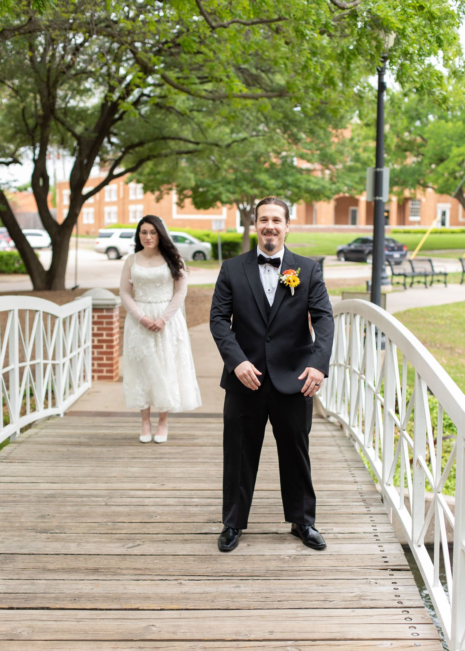 A couple stands on a white bridge during their wedding photoshoot in a park setting.