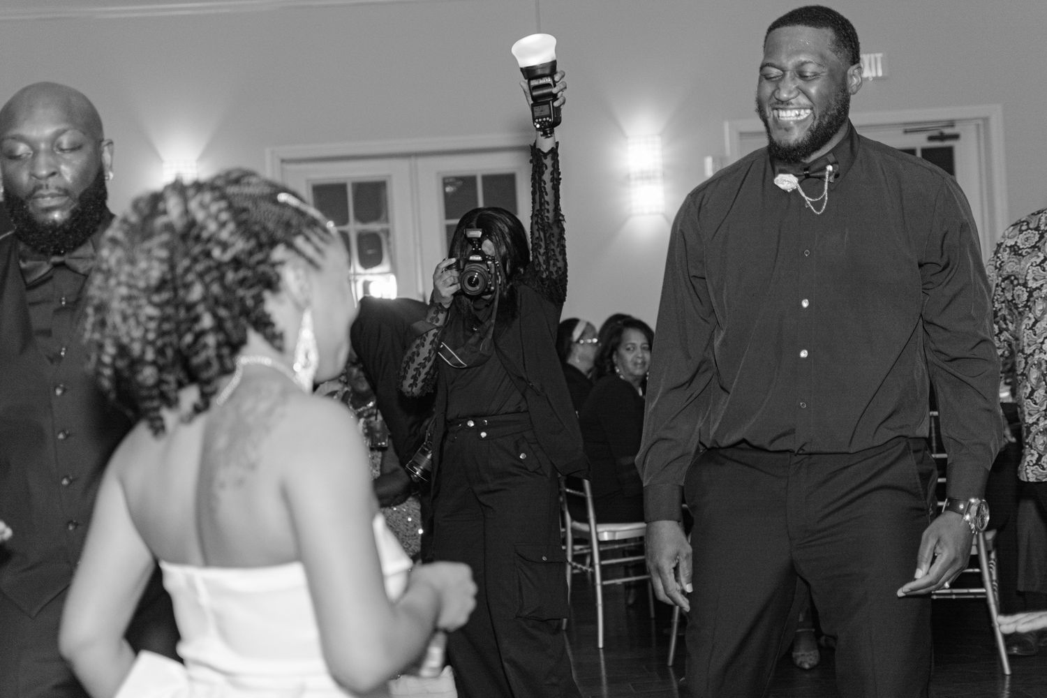 Guests celebrate and dance joyfully at a wedding reception in black and white photo.