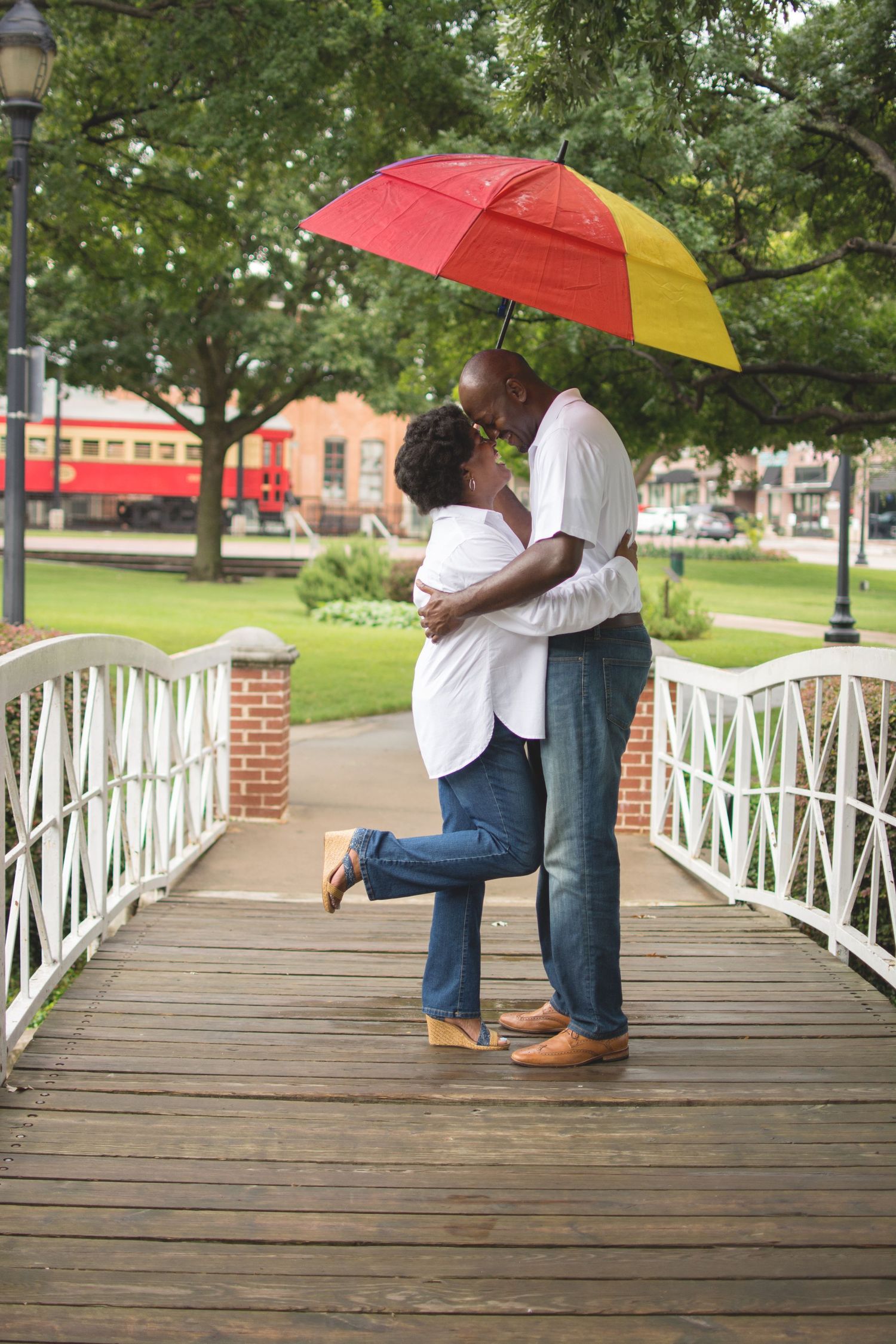 African American couple embracing and kissing under a red and yellow umbrella on a wooden bridge.