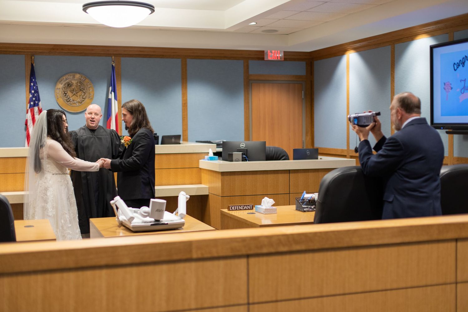 A courthouse wedding ceremony being documented by photographers as the couple stands before the judge.