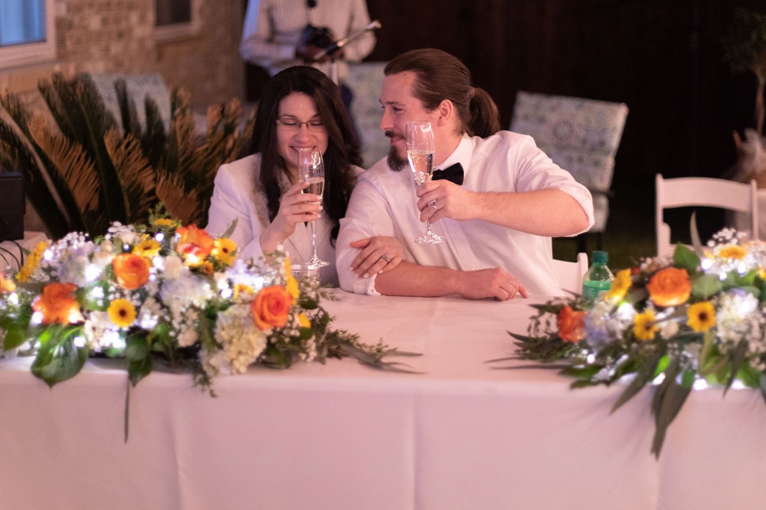 A couple seated at a decorated wedding table with colorful floral arrangements.