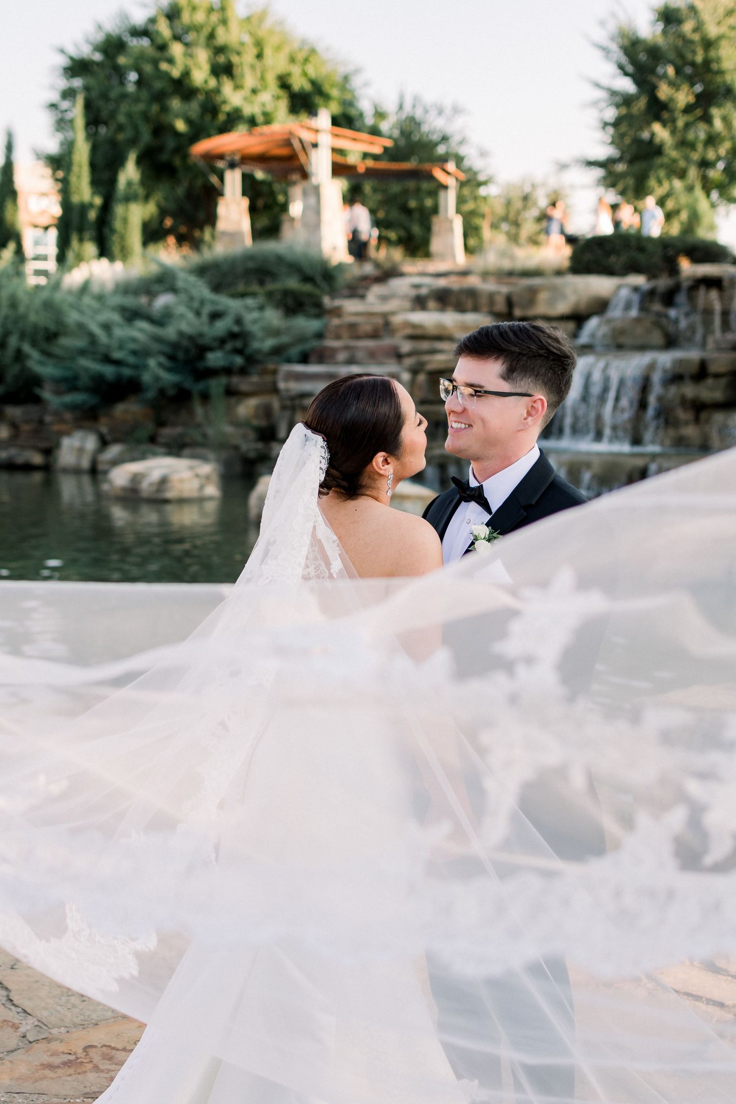 Bride and groom share a romantic moment near a waterfall as her veil billows in the wind.