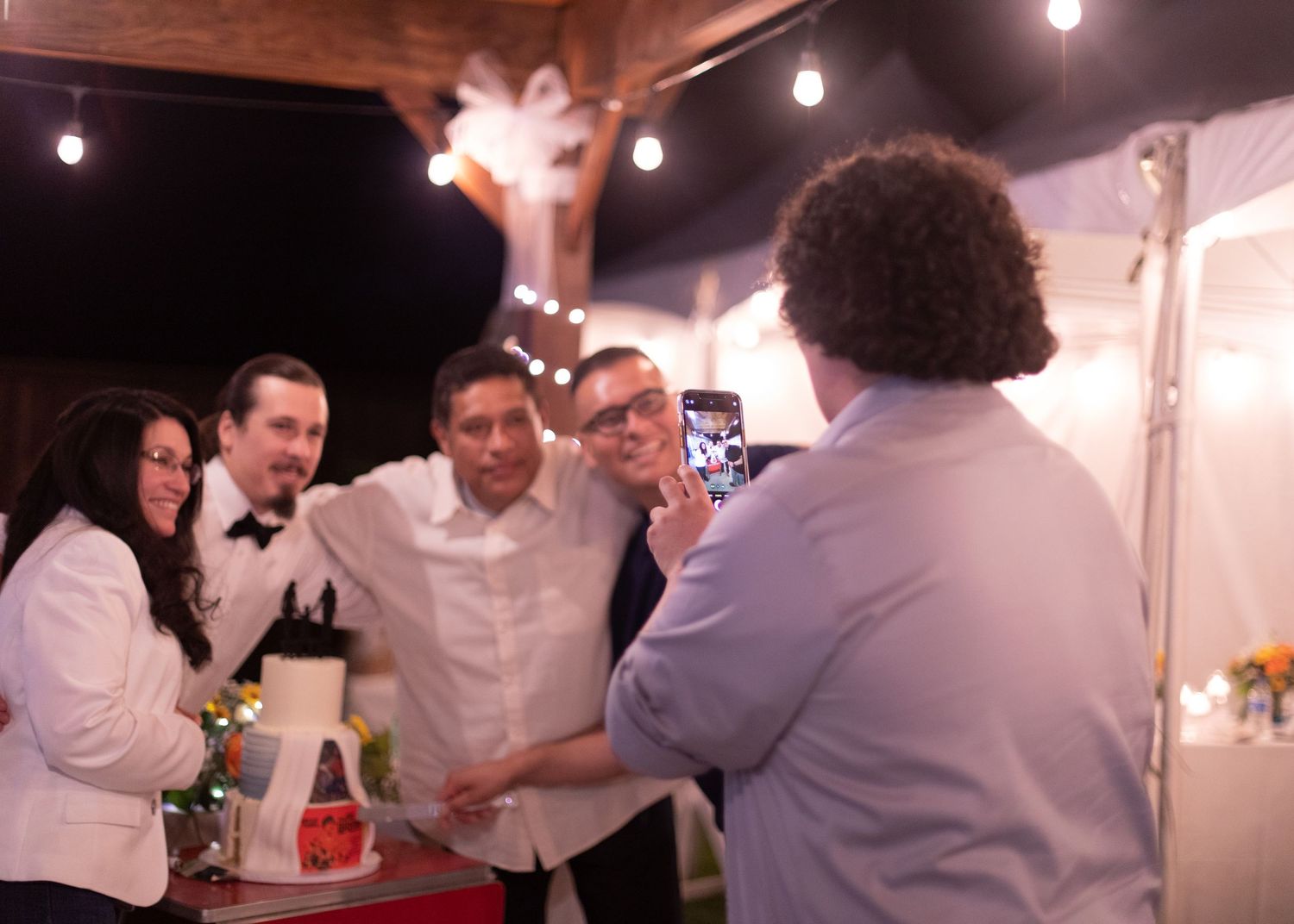 Group gathered around a phone at an evening reception with string lights.