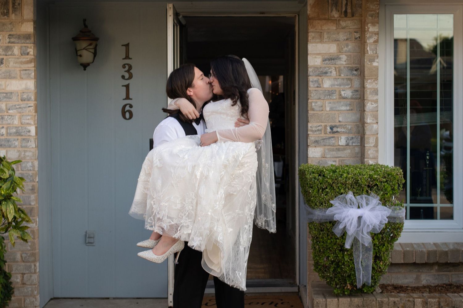 Traditional wedding threshold carry pose at front door of brick house.