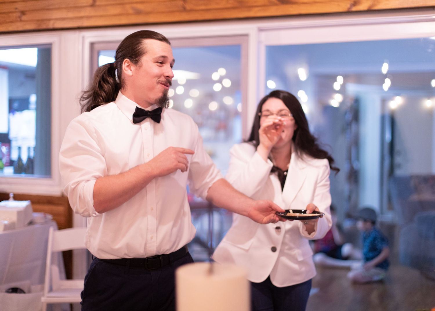 Two people having an animated discussion while eating cake at a reception.