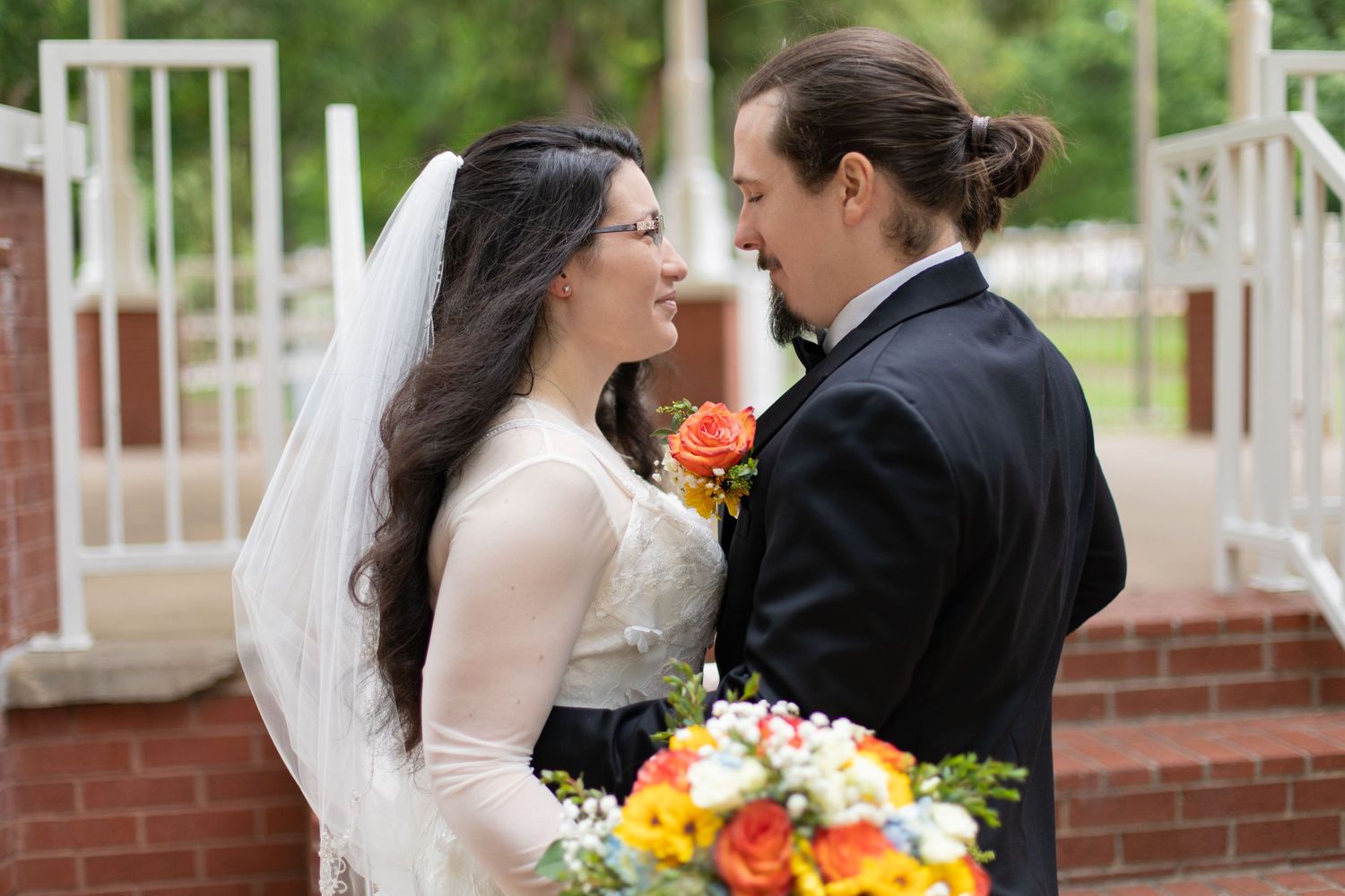A romantic wedding moment captured between newlyweds with colorful bouquet on brick steps.