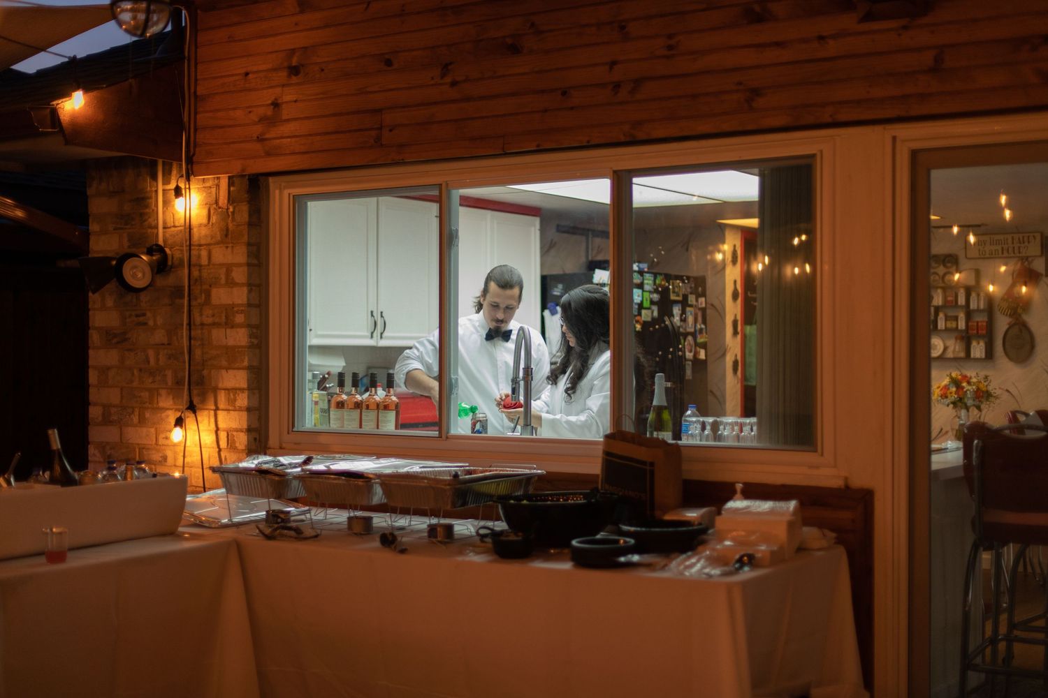 View through a window of a warmly lit restaurant interior with string lights.