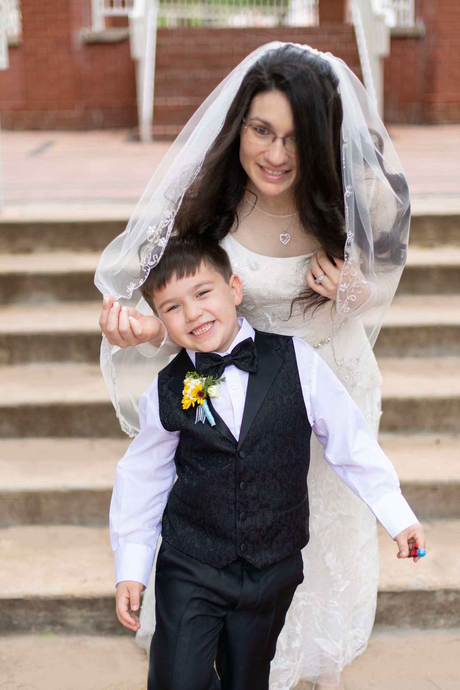 Candid wedding portrait on brick steps with bride and ring bearer sharing joyful moment.