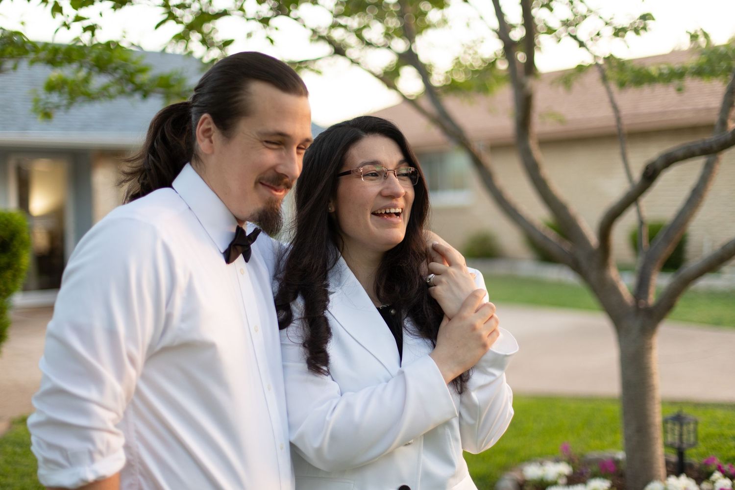 Candid laughing moment in matching formal wear under tree branches.