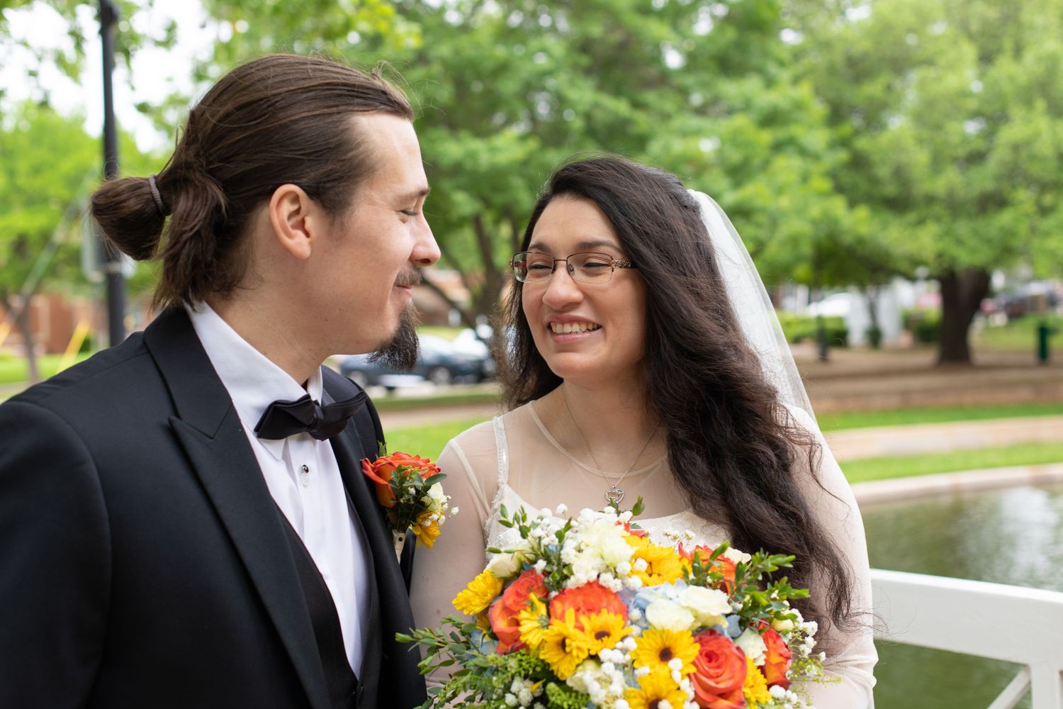 A couple shares a tender moment on a white bridge with vibrant orange and yellow bouquet.
