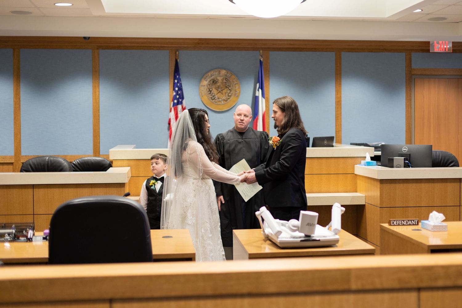 Judge performing marriage ceremony for couple in courtroom setting.