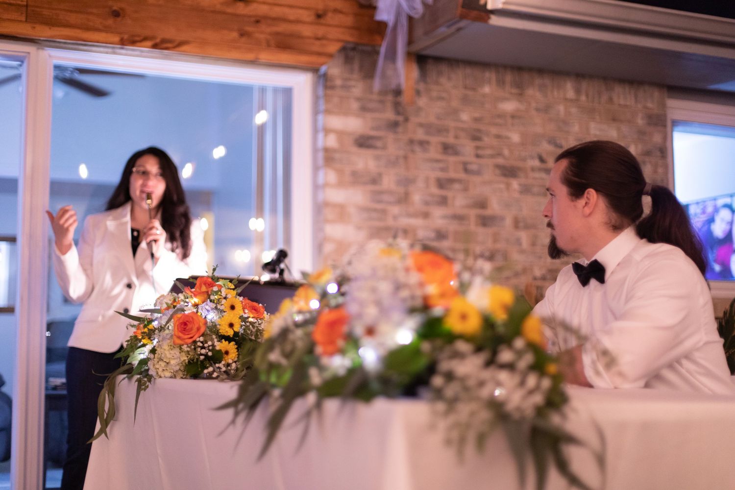 A wedding speech being delivered at a decorated reception venue with brick walls and flowers.