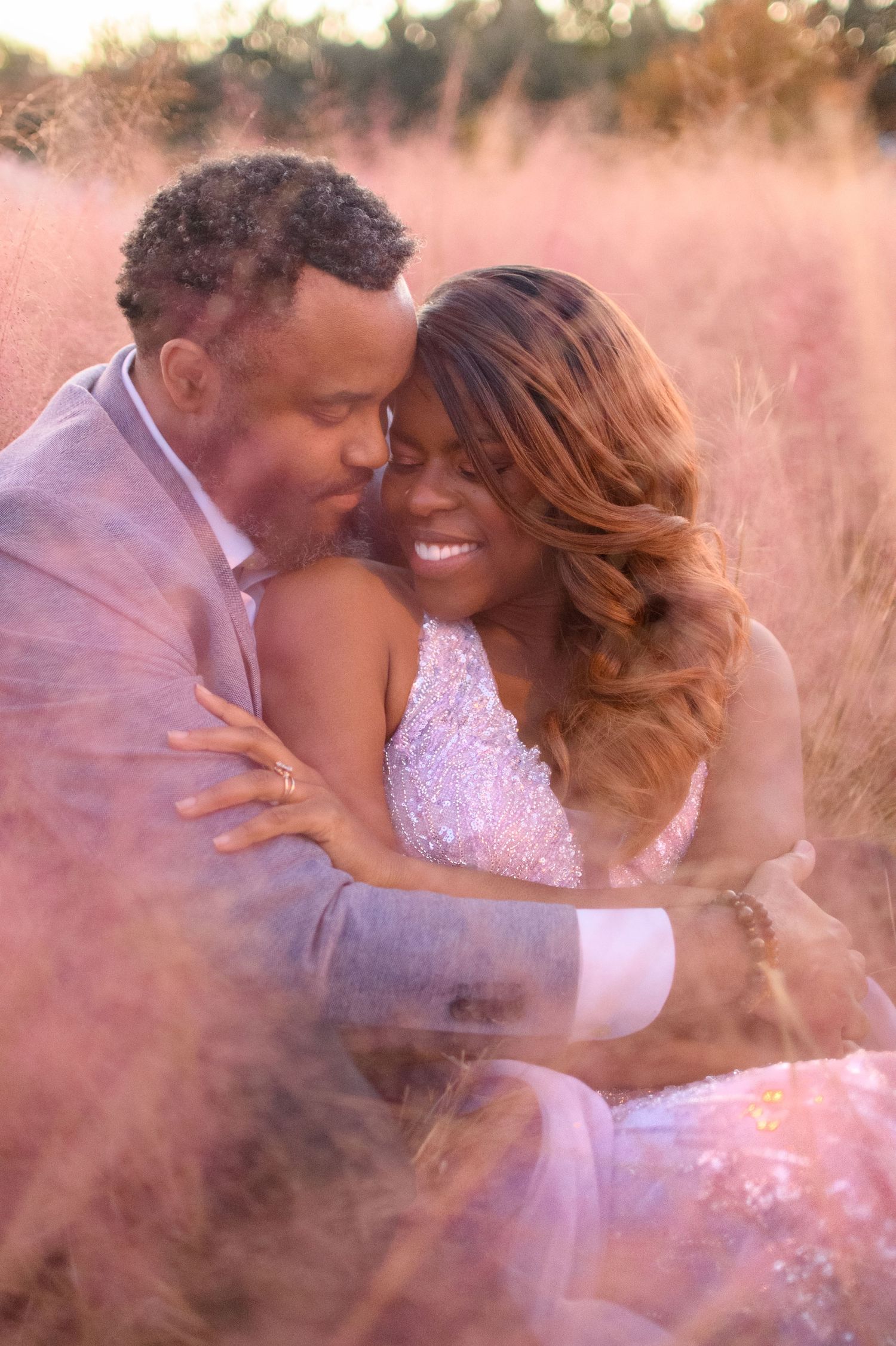 A joyful couple embraces romantically in a field of pink ornamental grass, wearing elegant wedding attire.