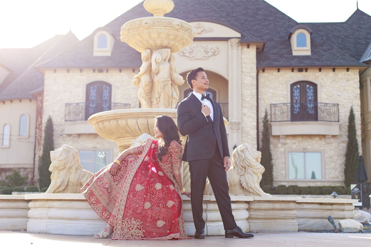 Indian bride and groom pose romantically in front of a grand fountain at a luxury estate.