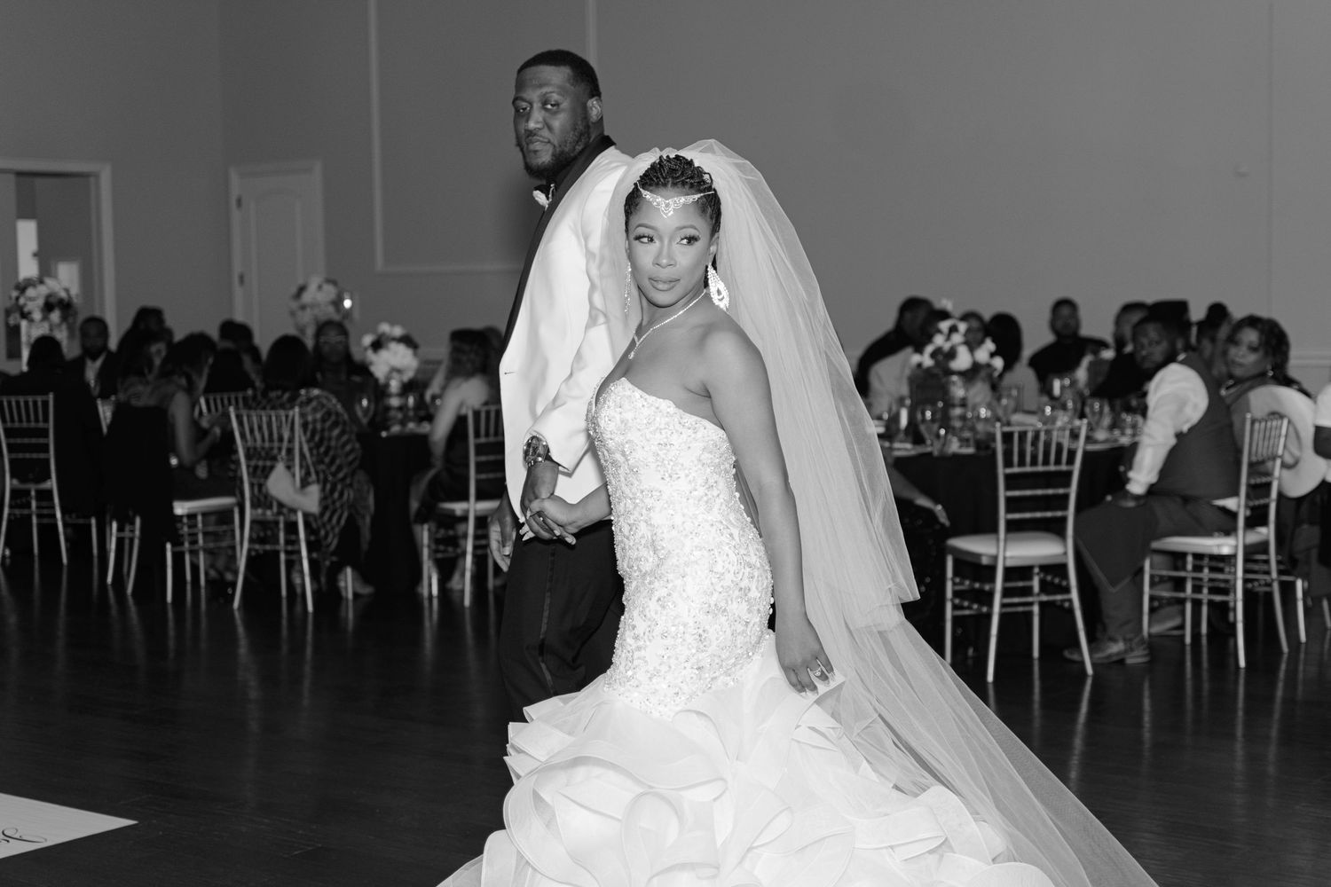 Elegant black and white portrait of bride in mermaid gown and groom standing in wedding reception hall.