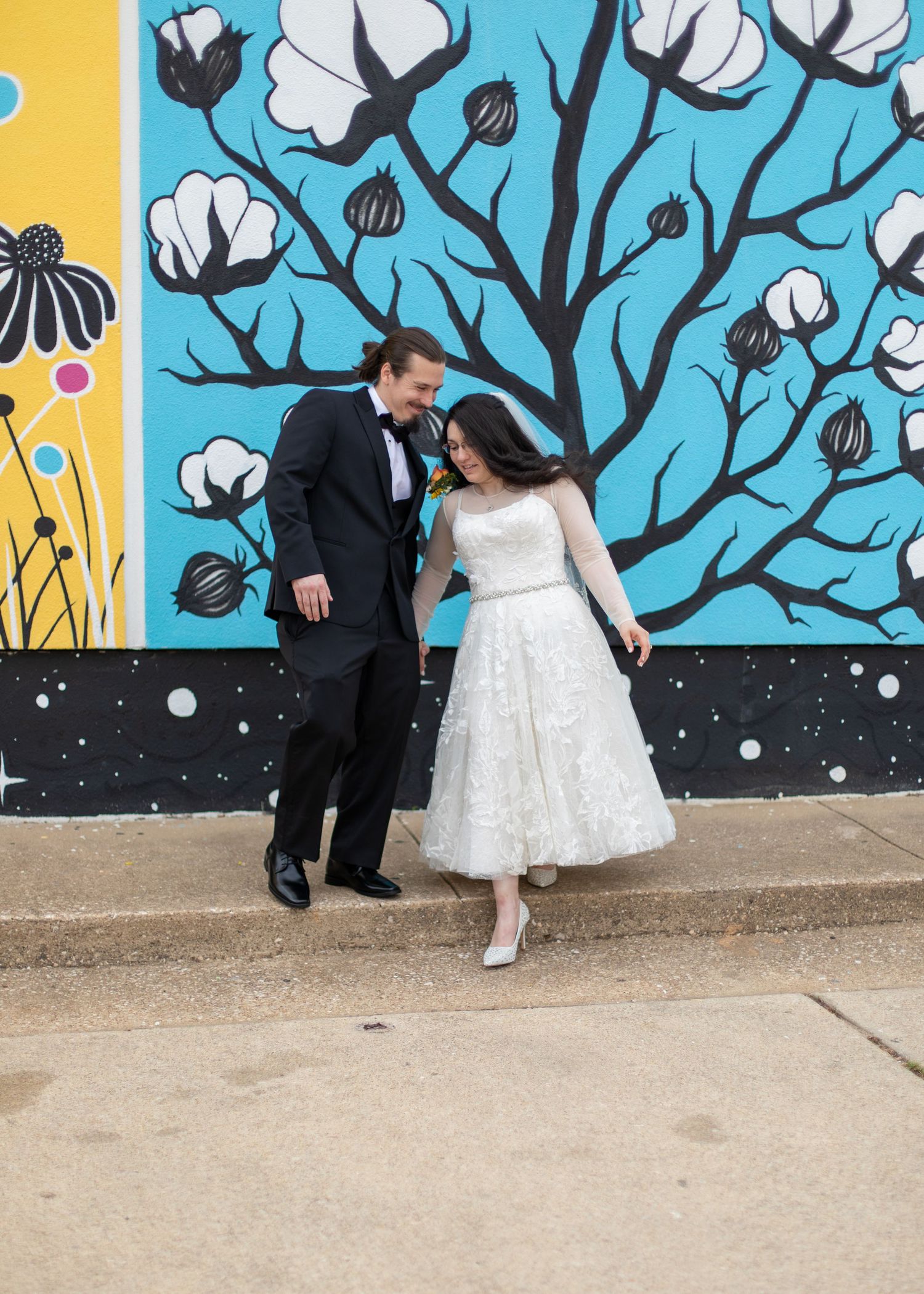 A couple shares a joyful moment in front of an artistic mural with cotton plants.