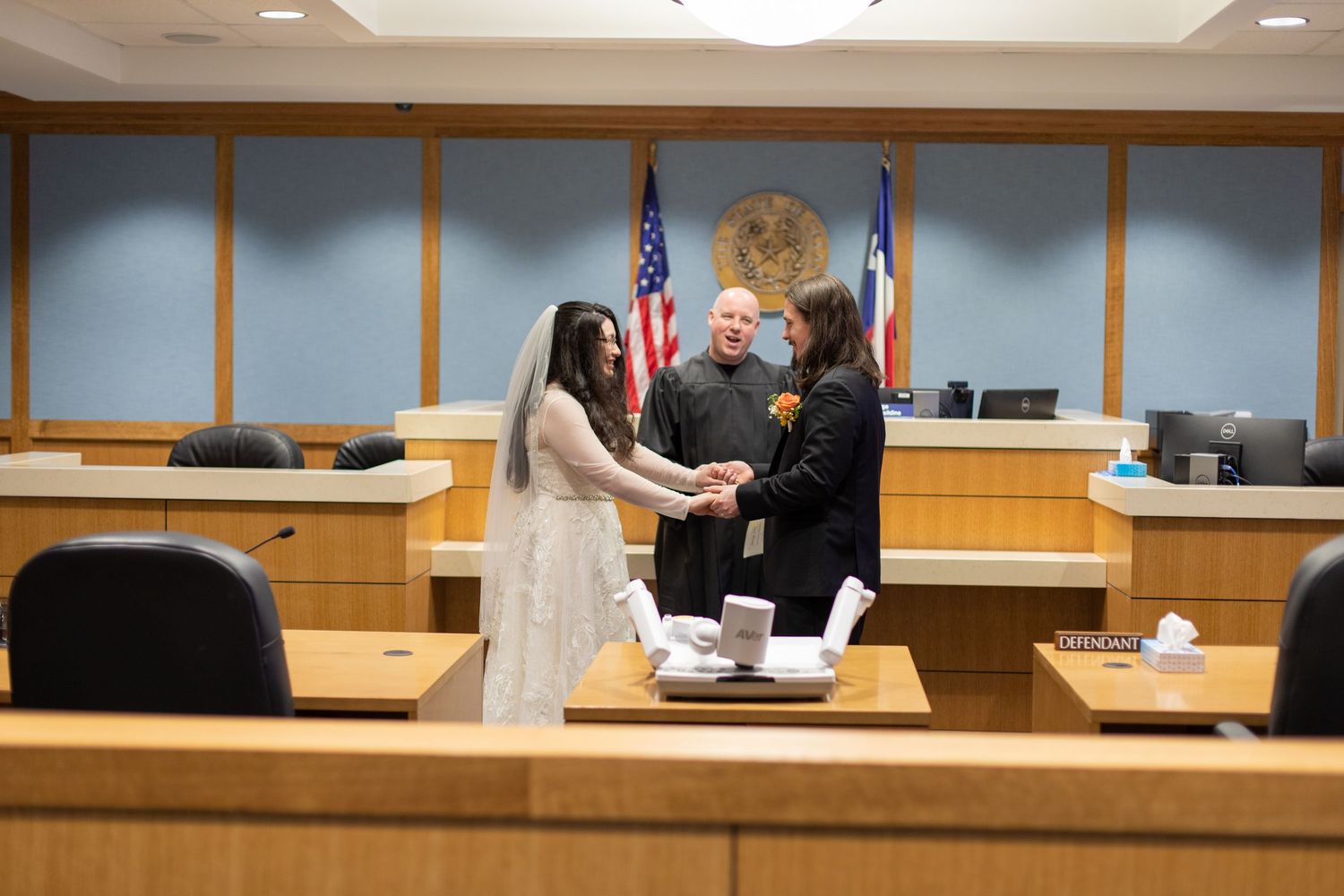 A couple holds hands during their courthouse wedding ceremony with American flag in background.