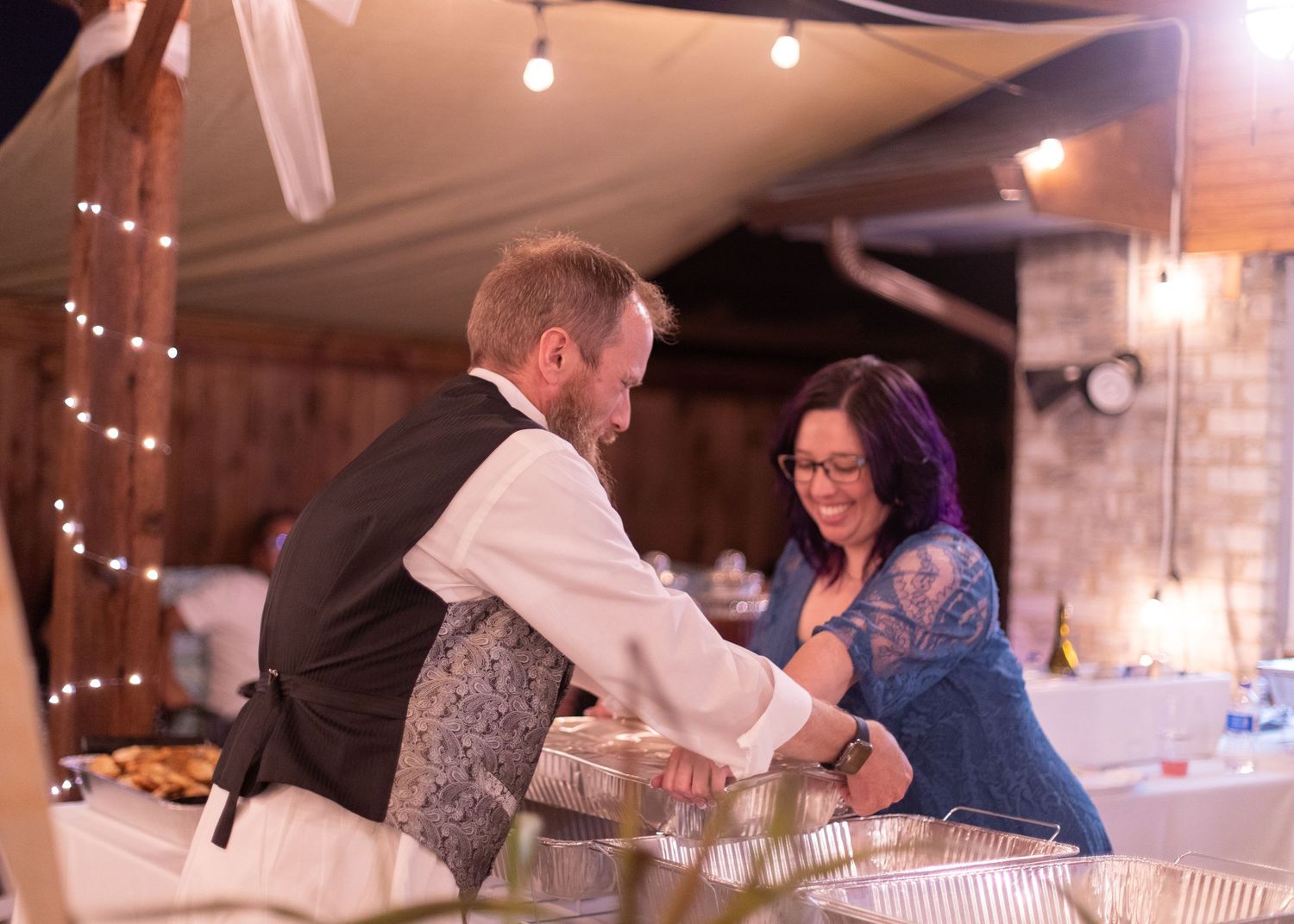 Gift exchange moment at a reception under string lights and fabric draping.