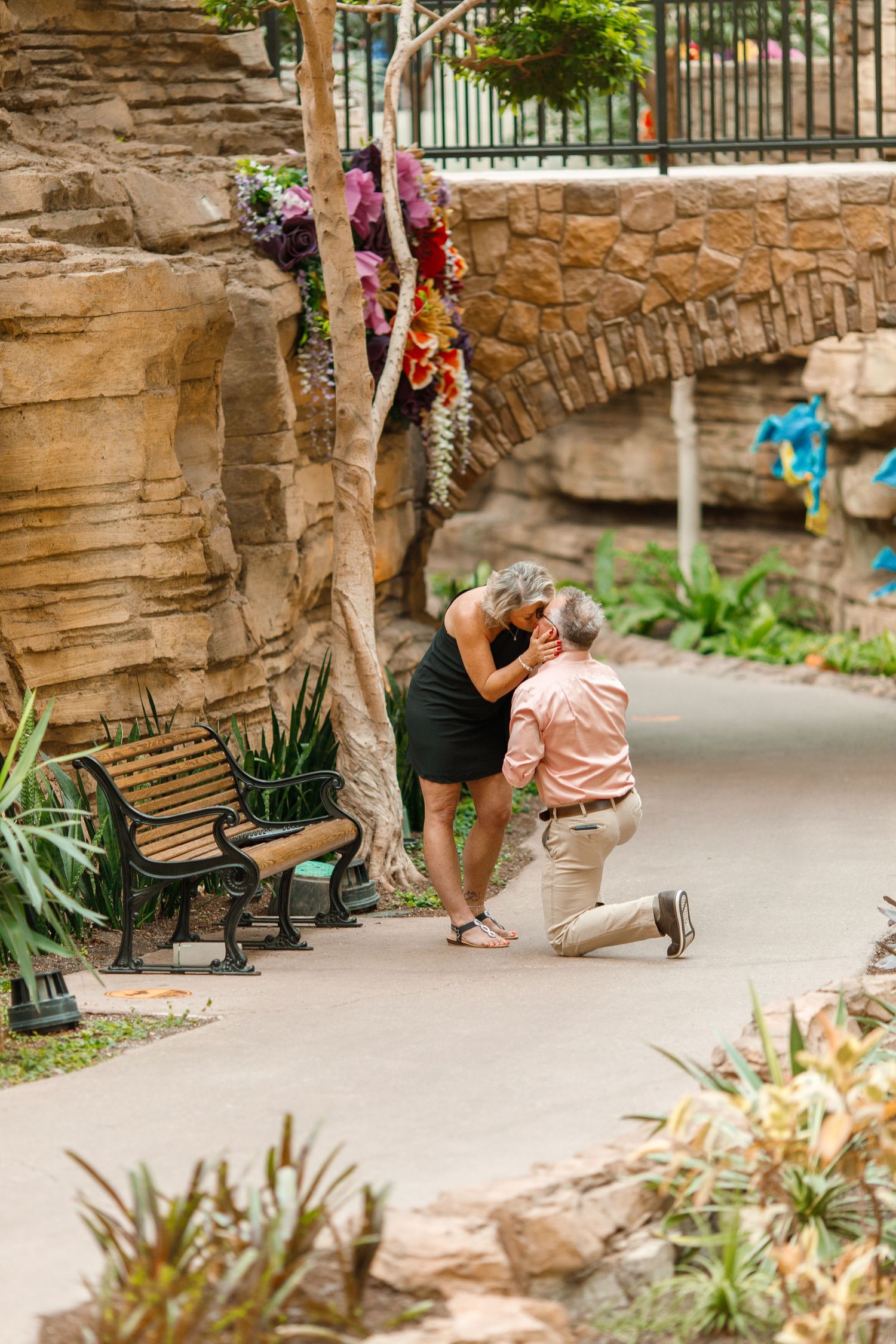 Romantic proposal scene on stone pathway with decorative flowers hanging overhead.