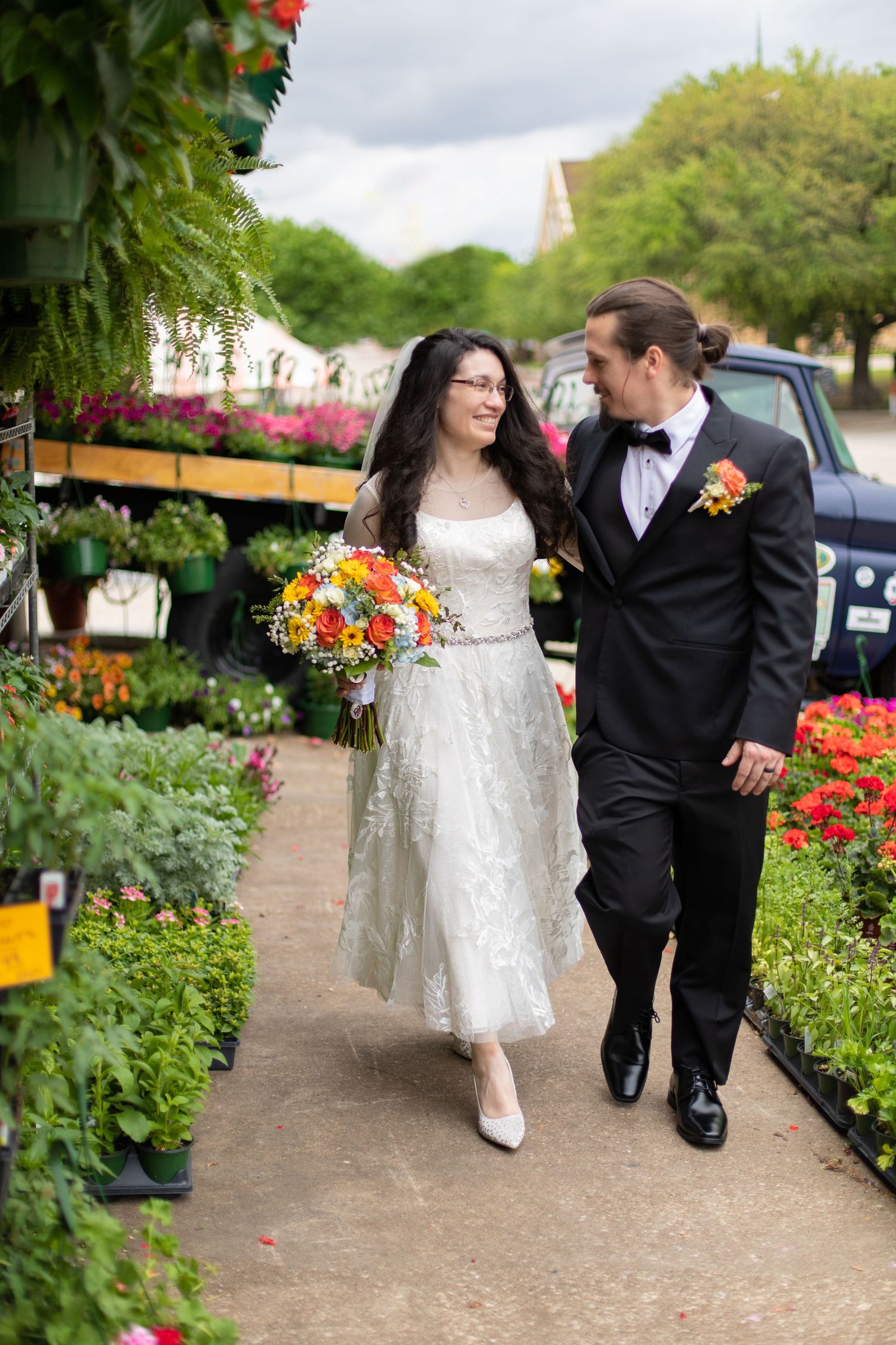A couple walks together on a pathway among vibrant flower displays at a garden center.
