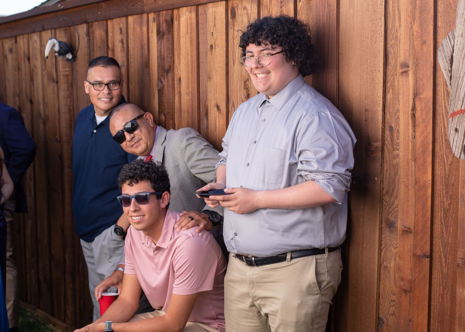 Casual group gathered against wooden fence wearing sunglasses and casual attire.