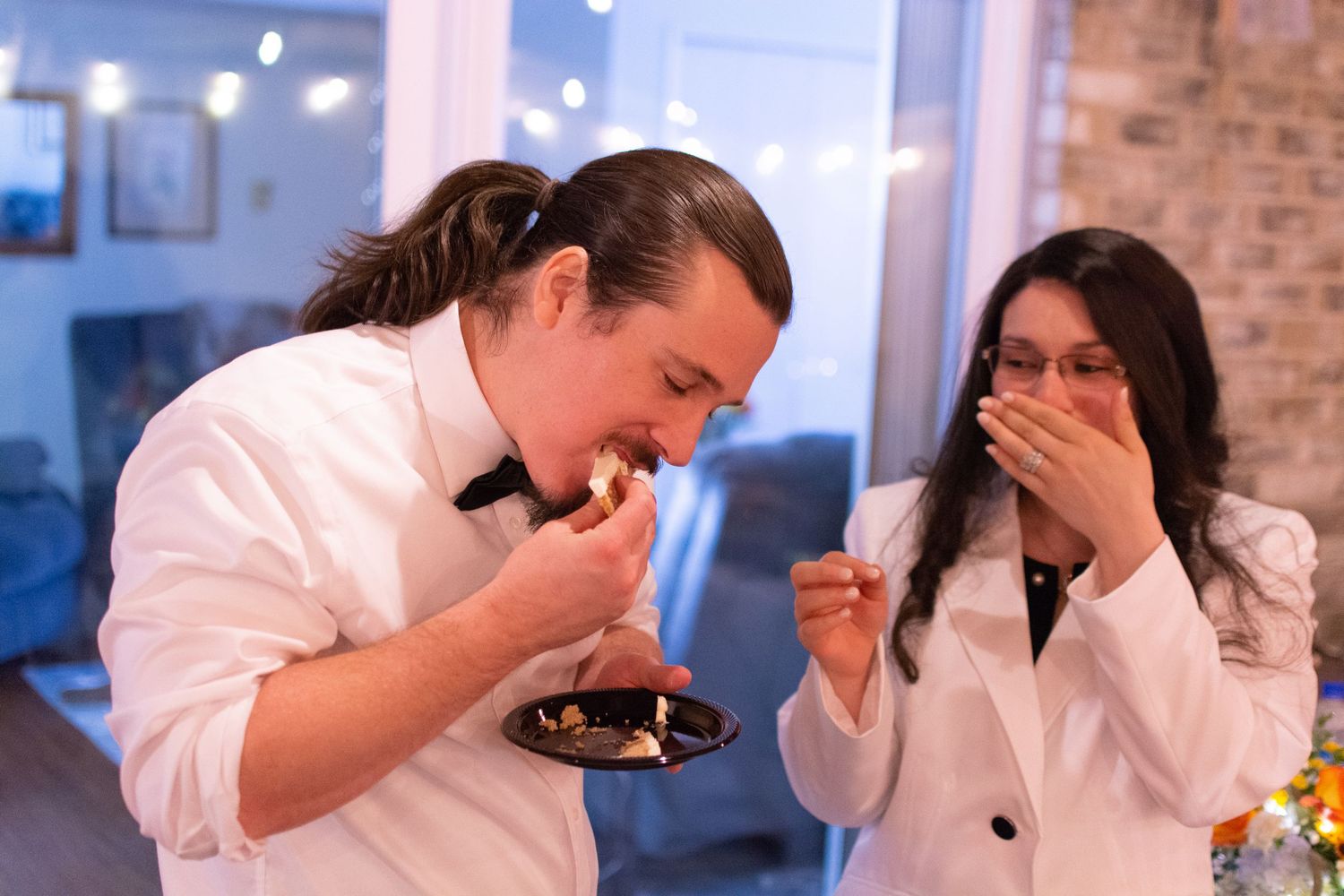 Two people laughing while sampling desserts at an event.