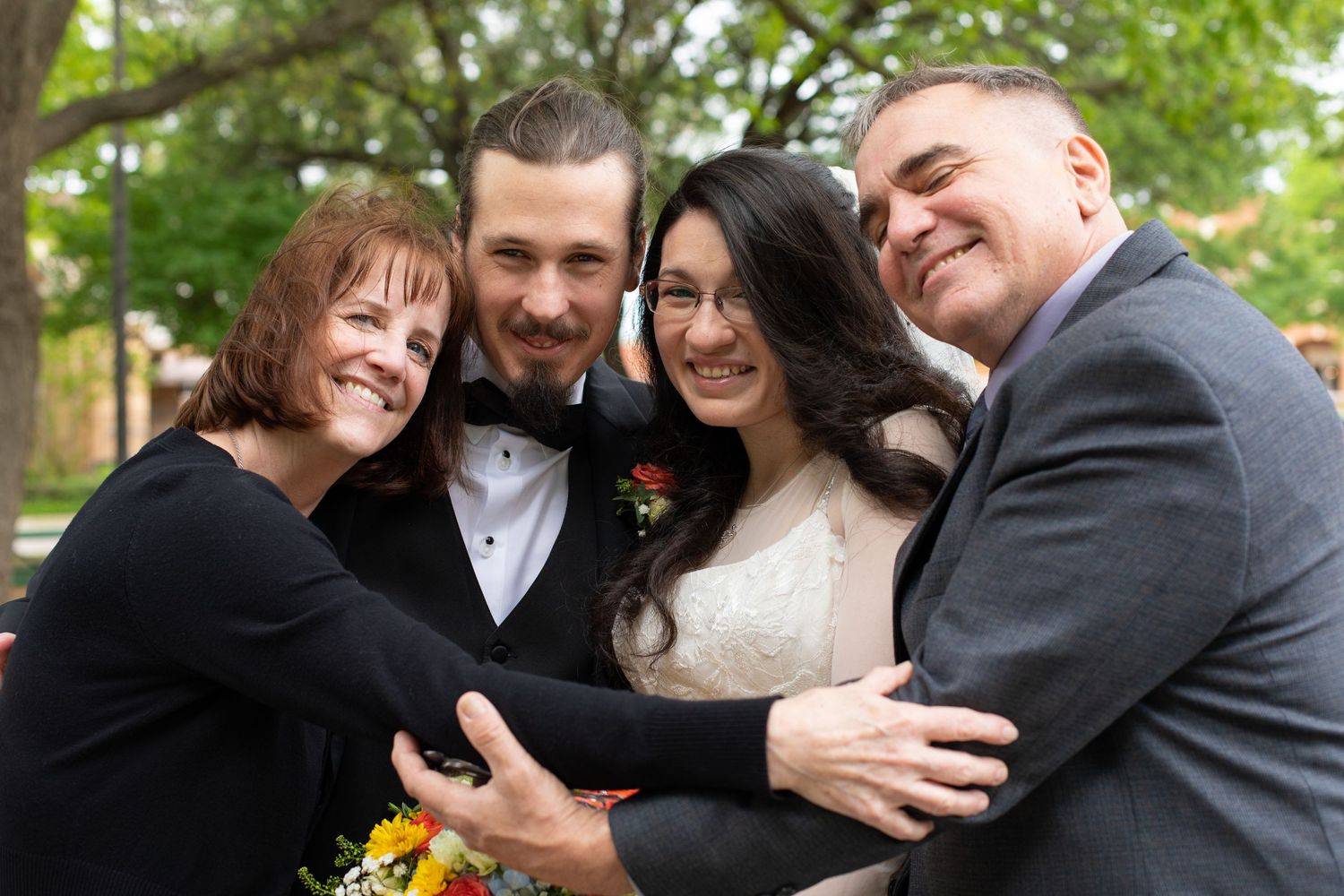 A joyful group embrace during wedding photos in an outdoor setting.