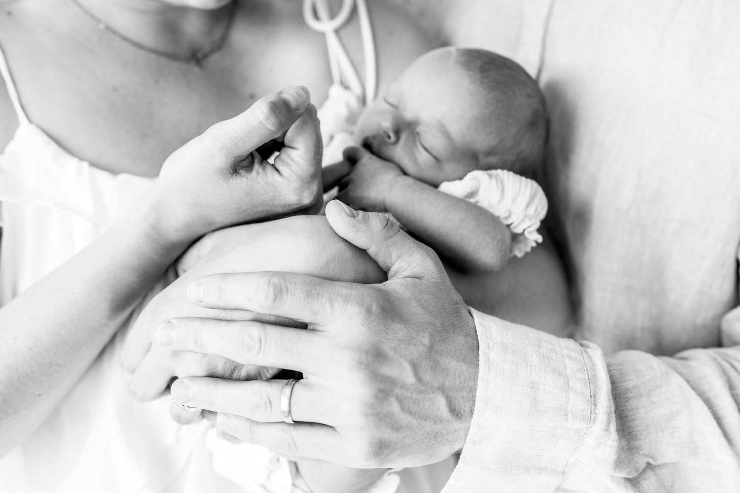 Black and white photo of parents cradling their newborn baby, mother wearing wedding ring.