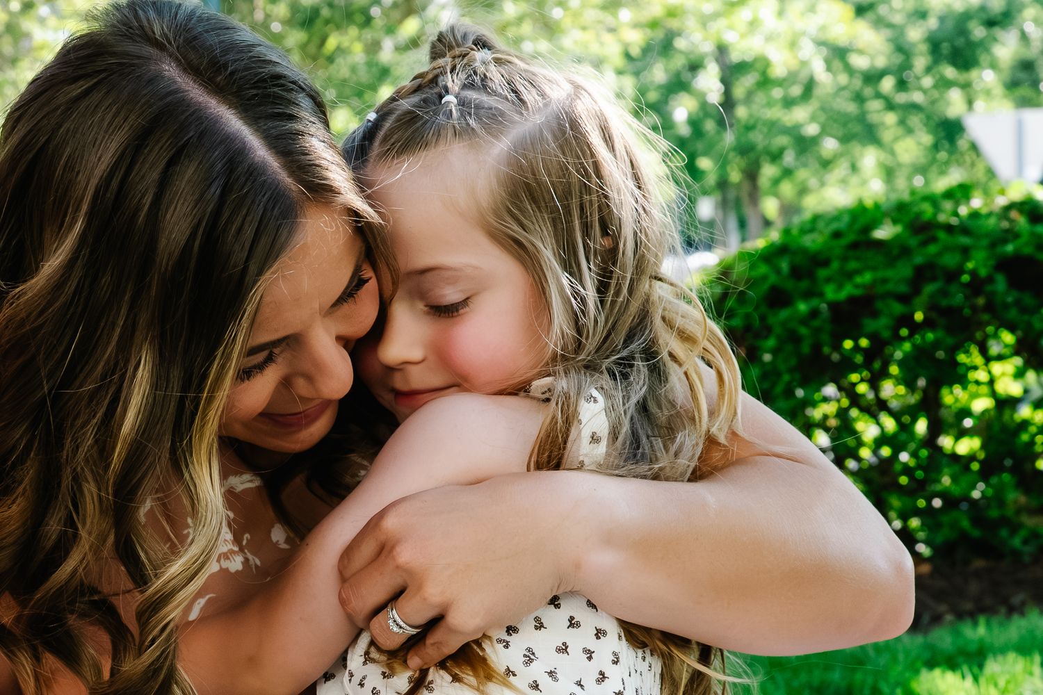 Tender moment of a mother hugging her young blonde daughter outdoors in a green garden.