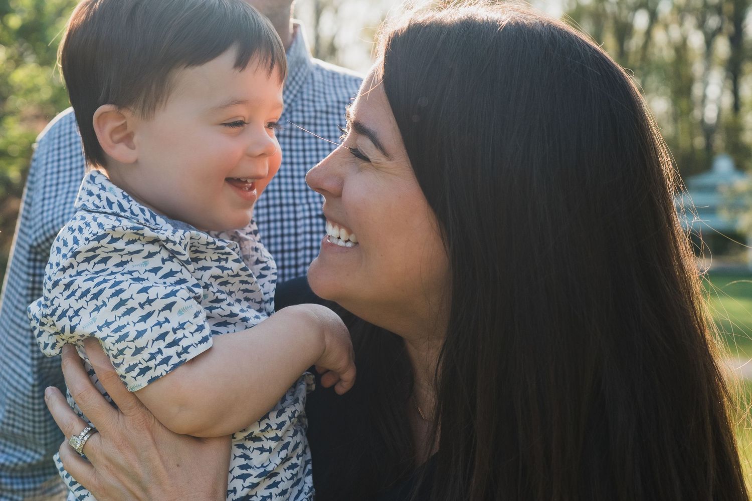 Happy mother holding smiling toddler face-to-face in a sunny outdoor setting.